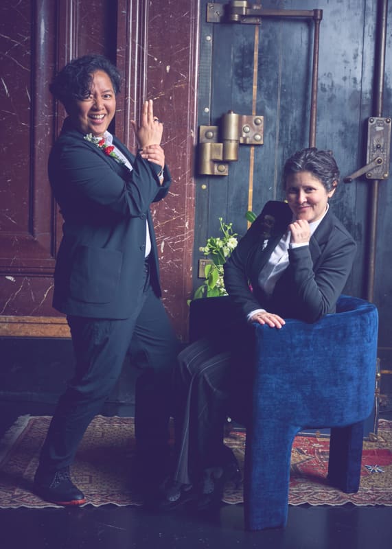 Holly and Rosalie in dark suits at a blue door, posing