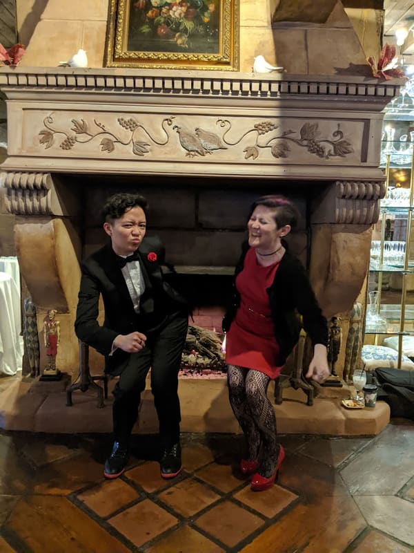 Holly and Rosalie in formalwear in front of an ornate fireplace