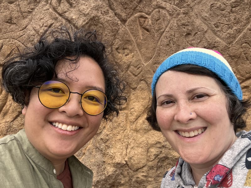 Holly and Rosalie in yellow glasses and a blue hat against carved stone